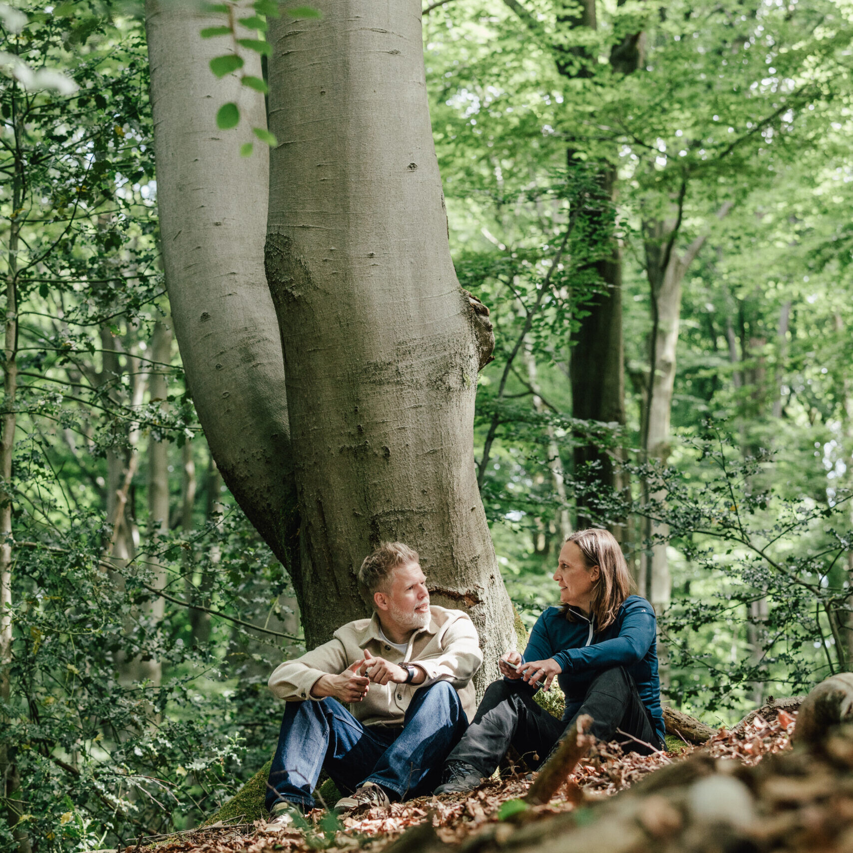 Christiane sitzt mit einem Klienten im Wald und führt ein Coaching-Gespräch